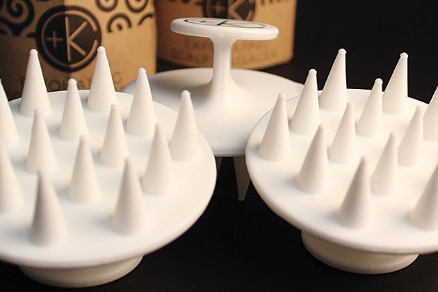 Close-up of three Cult and King Exfoliating Scalp Massagers with pointed bristles in front of cylindrical Cult and King cardboard boxes.