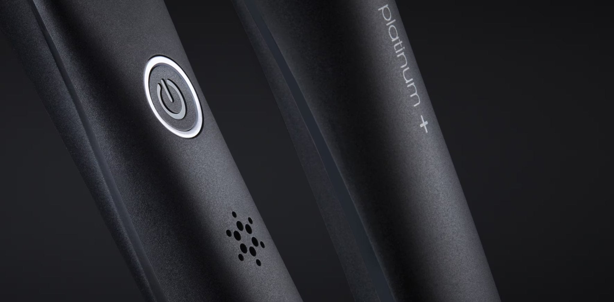 Close-up of a black GHD PLATINUM+ STYLER - 1" FLAT IRON with a power button and “platinum+” text visible on the device, highlighting its smart styler capabilities for personalized styling.