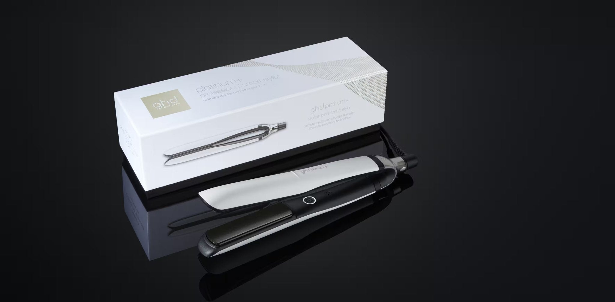 A black and silver GHD PLATINUM+ STYLER - 1" FLAT IRON lies next to its white packaging box with "GHD" branding, all set against a dark reflective surface, ready to deliver personalized results.