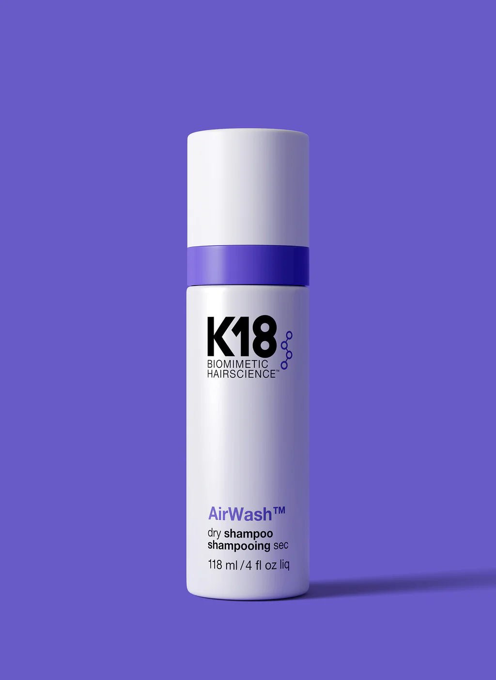 A white and purple bottle of K18 AirWash Dry Shampoo by Simply Colour Hair Salon Studio & Online Store, utilizing odorBIND biotechnology to reduce oil, containing 118 ml (4 fl oz). The bottle stands against a solid purple background.