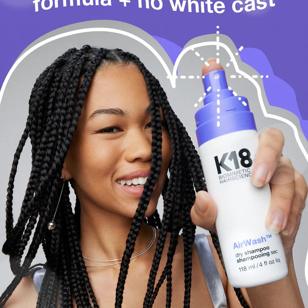 A person with braided hair holds a bottle of K18 AirWash Dry Shampoo from Simply Colour Hair Salon Studio & Online Store. Text above reads, "non-aerosol scalp-friendly formula + no white cast, reduces oil with odorBIND biotechnology".