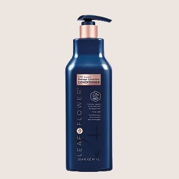 A dark blue bottle of Leaf and Flower Damage Correction Conditioner with a pump dispenser, featuring a color-safe, plant-based formula, set against a light background. Multiple sizes available.