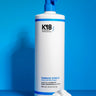 A 930 ml bottle of K18 Hair Repair K18 Damage Shield pH Protective Conditioner - Multiple Sizes, enriched with K18PEPTIDE™, stands beside a dollop of the product against a blue background, promoting hair health.