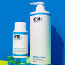 Two white bottles of K18 DAMAGE SHIELD pH Protective Shampoo - Multiple Sizes by K18 Hair Repair are displayed against a blue background. One bottle is 250 ml and the other is 930 ml, both labeled with volume and product name. Ideal for daily use, this cleansing shampoo ensures your hair stays fresh and vibrant.